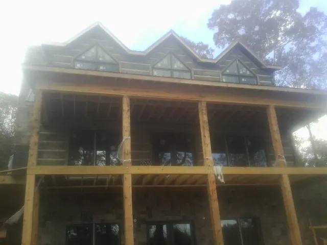 Dormers and porch framing on a large log home under construction — Roof Coating work by our crew in Malta