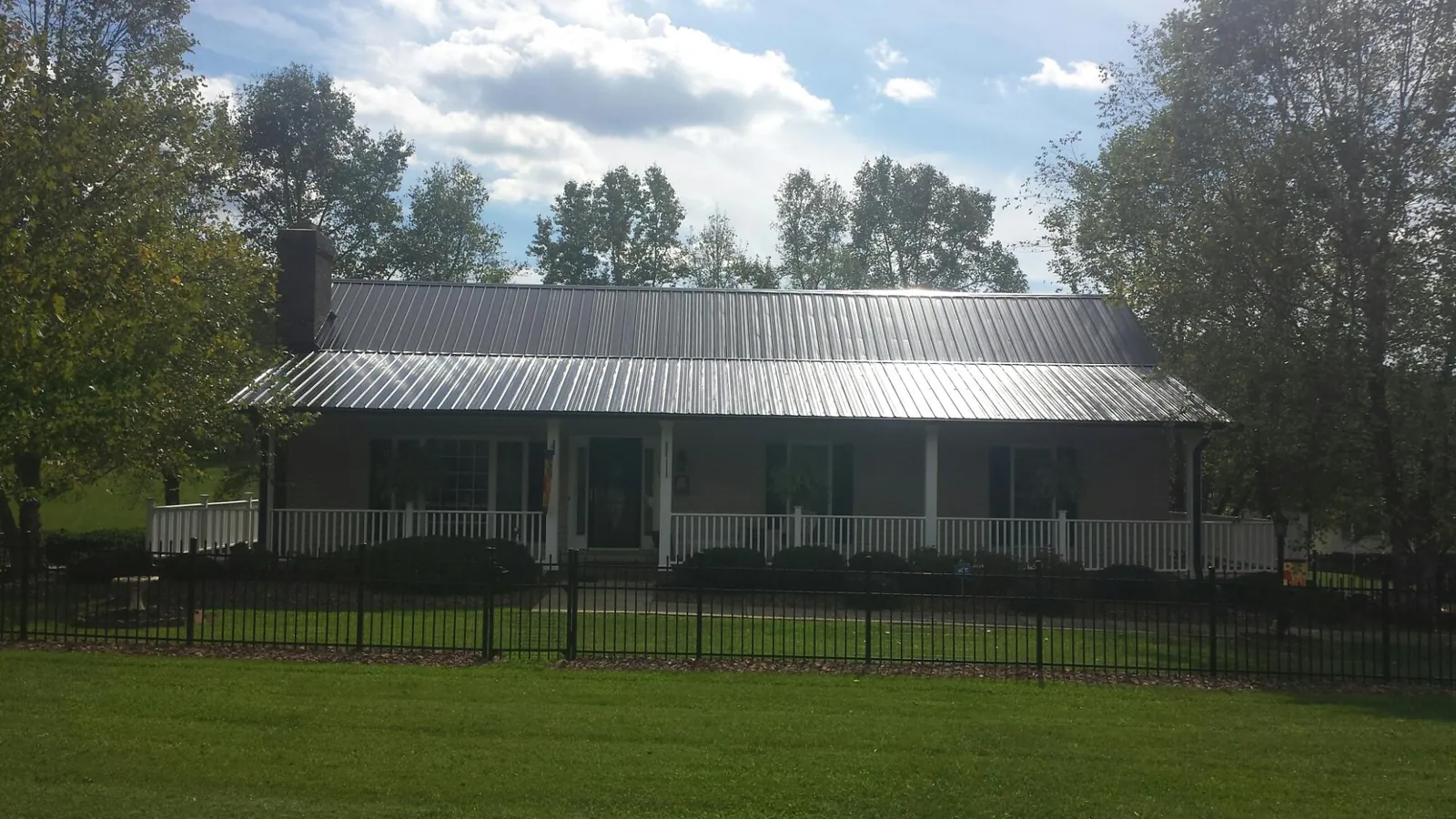 Gray metal roof on a brick ranch with a full width front porch — Gutter Guard Installation work by our crew in Malta