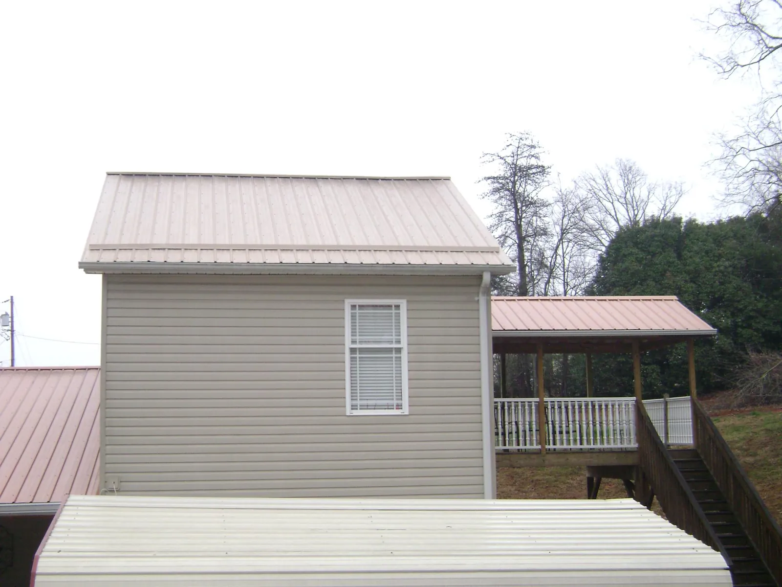Tan metal roofs on a two story addition and attached porch, from a Roof Replacement job in Malta